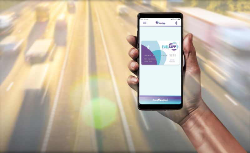 Hand holding smartphone displaying Certas Energy digital fuel card interface on road background.