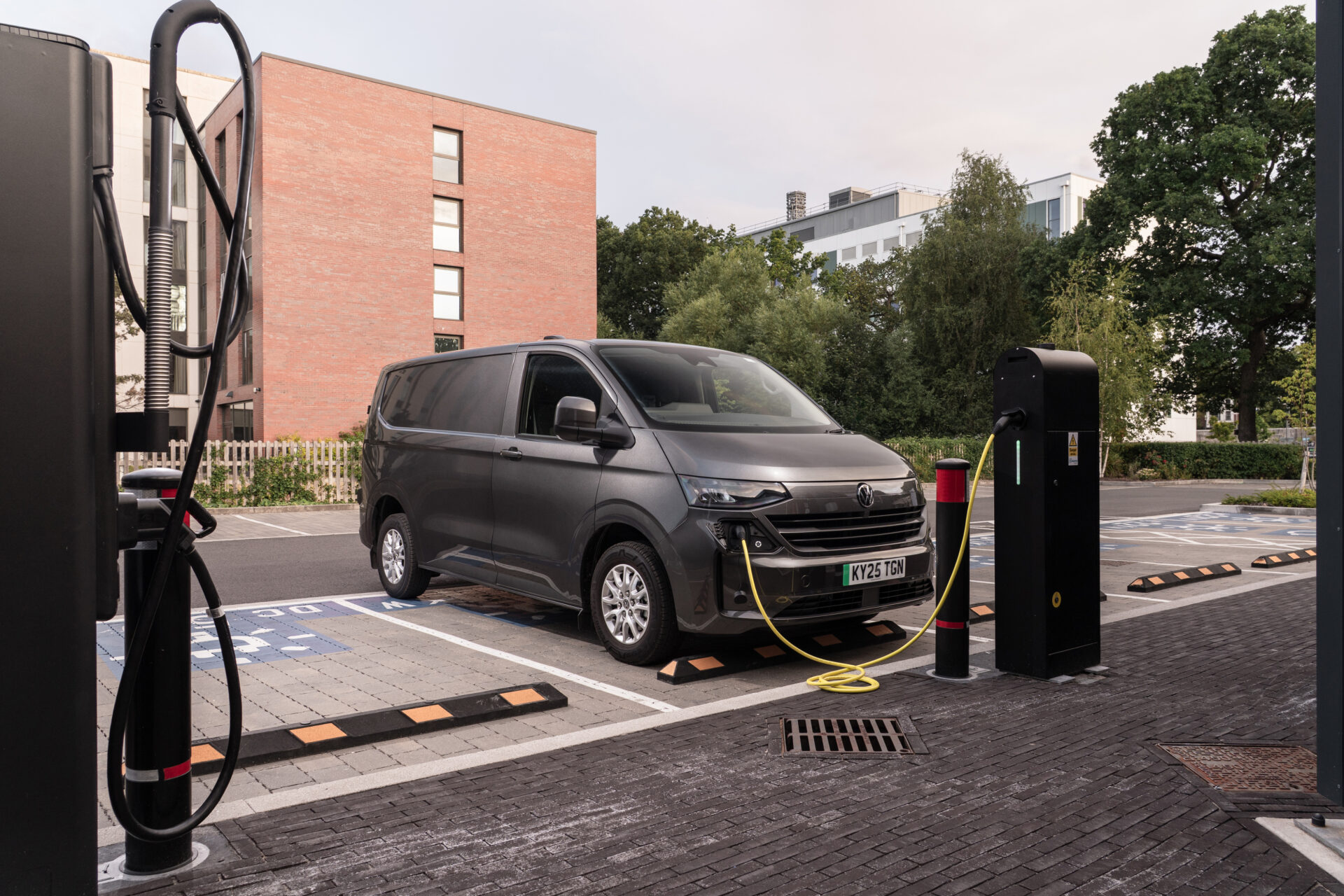 Electric van charging at public charging station with urban residential buildings in background.