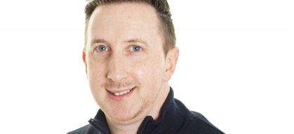 Man with short brown hair wearing black jacket against white background.
