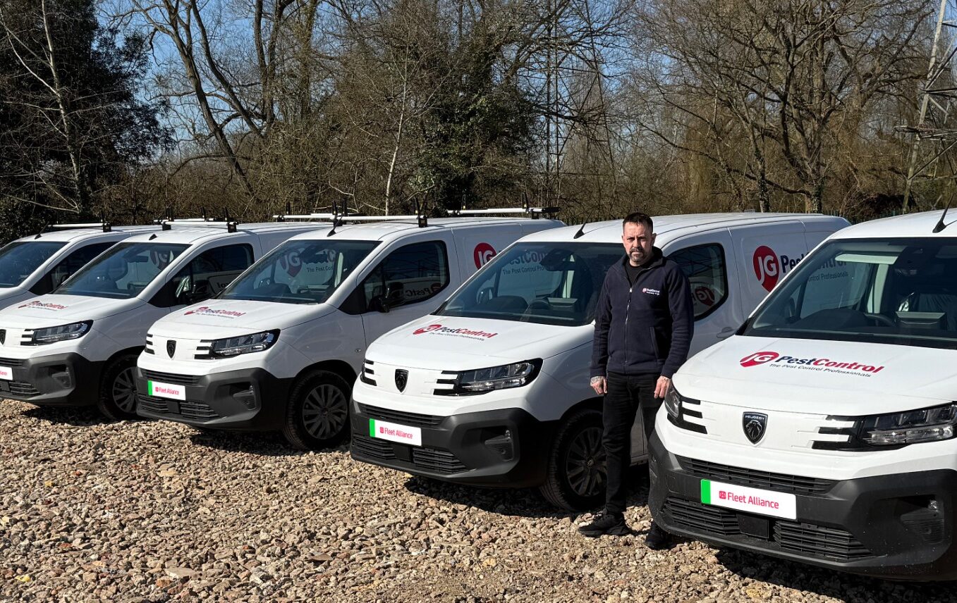 Man standing beside row of white Peugeot Partner vans branded with JG Pest Control livery, bare trees in background.