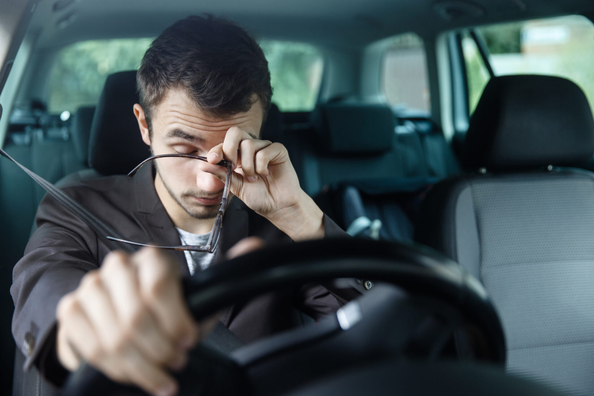 Tired driver rubbing eyes whilst gripping steering wheel inside car.