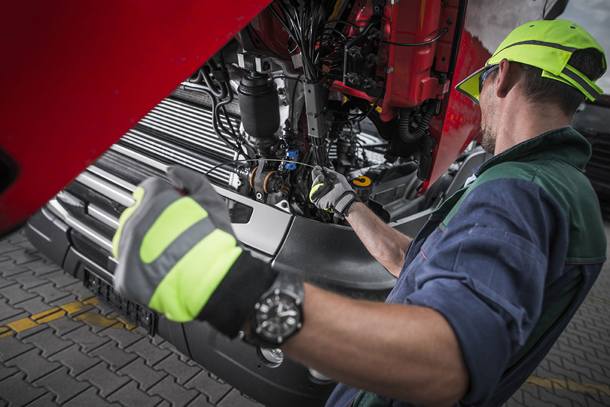 Mechanic in high-visibility clothing servicing engine components of red agricultural machinery.