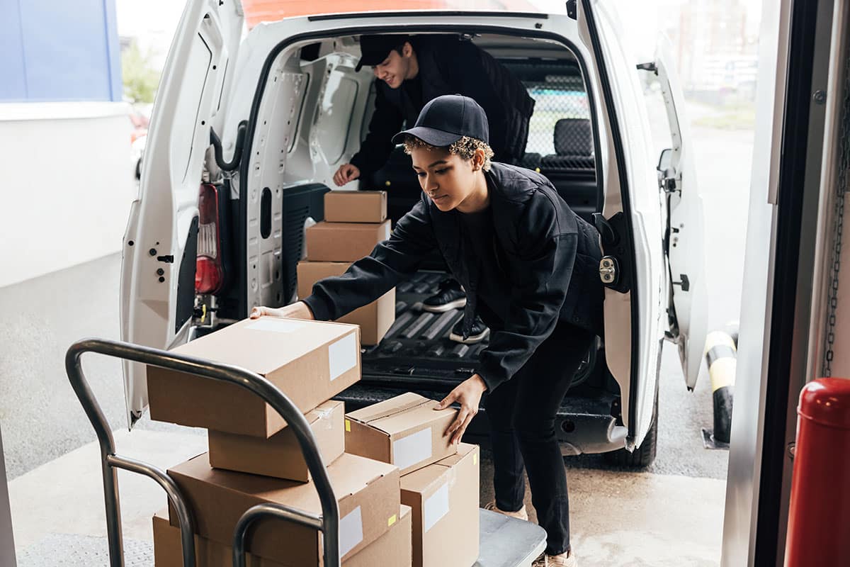 Delivery worker loading cardboard boxes onto a hand truck from a white van.