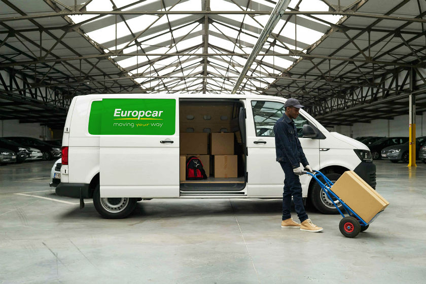 Man loading cardboard box onto hand truck beside white Europcar van in warehouse.