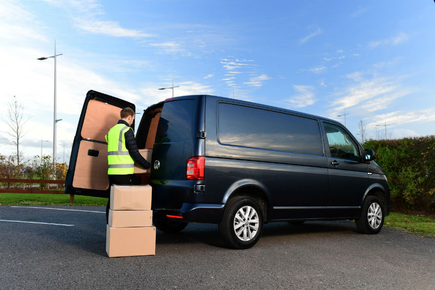 Delivery worker in high-visibility vest loading cardboard boxes into dark blue van with open side door.