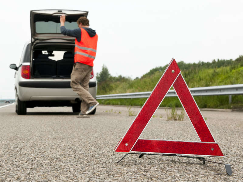 Breakdown warning triangle on motorway hard shoulder with person in high-visibility vest retrieving items from open van boot.
