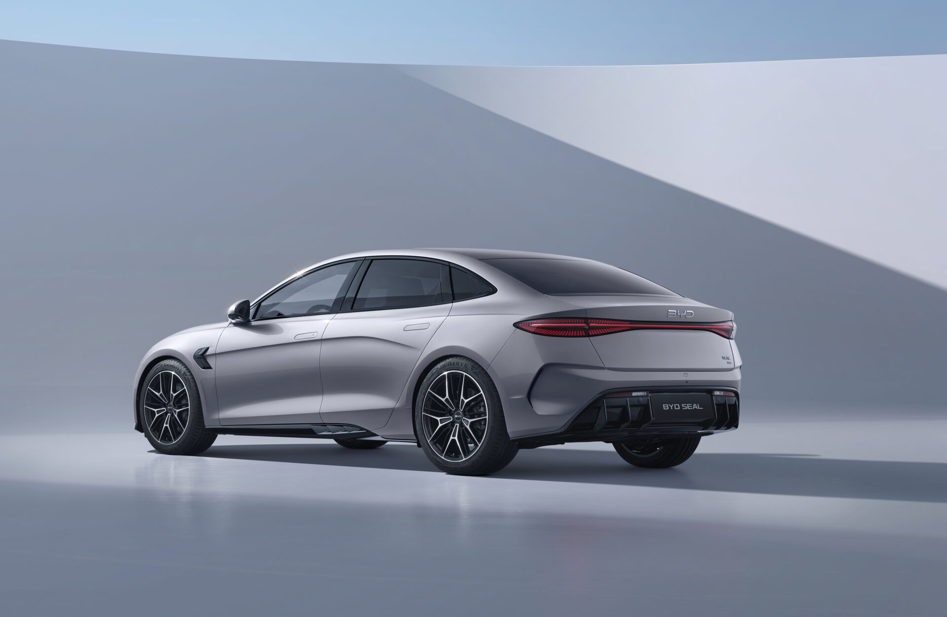 Silver BYD Seal saloon car shown in profile against curved grey and white architectural backdrop.
