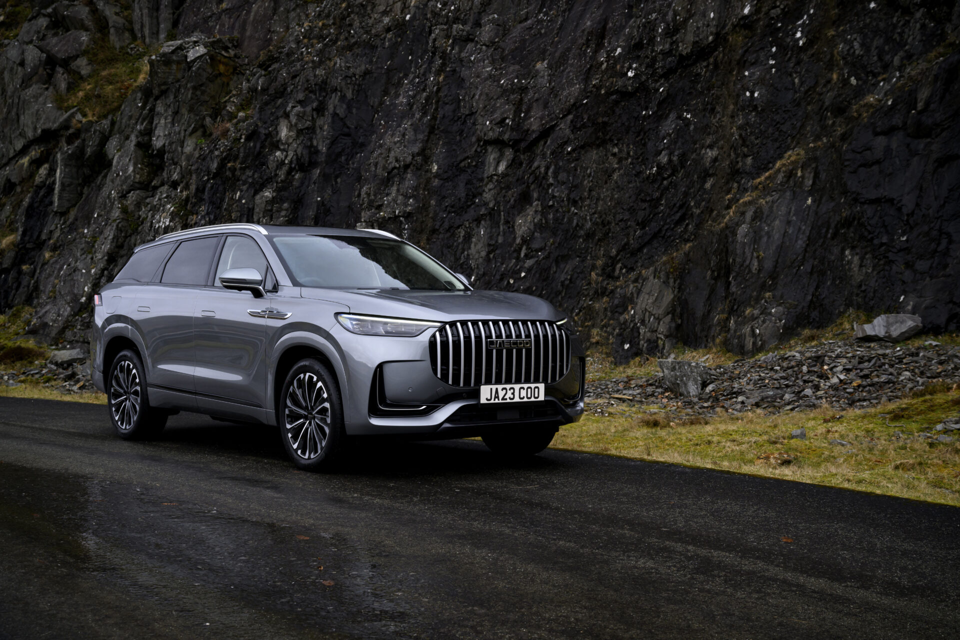 Silver JAECOO 8 SHS-P flagship SUV parked on dark tarmac against rocky cliff face.