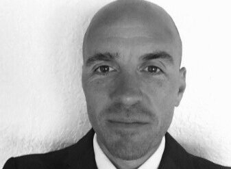 Bald man in business suit against white background, professional headshot.