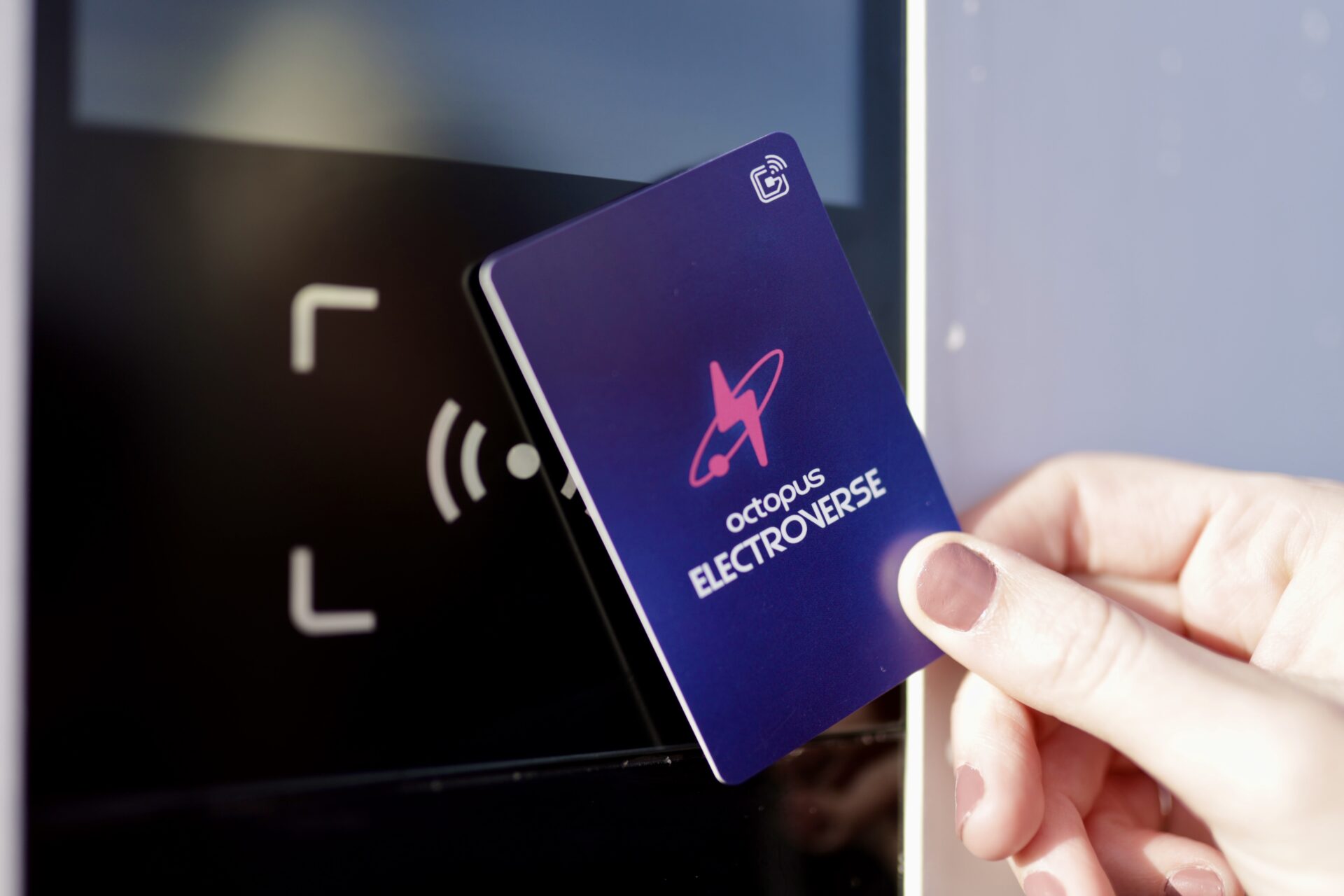 Hand holding purple Octopus Electroverse contactless card near charging point with wireless payment symbol.