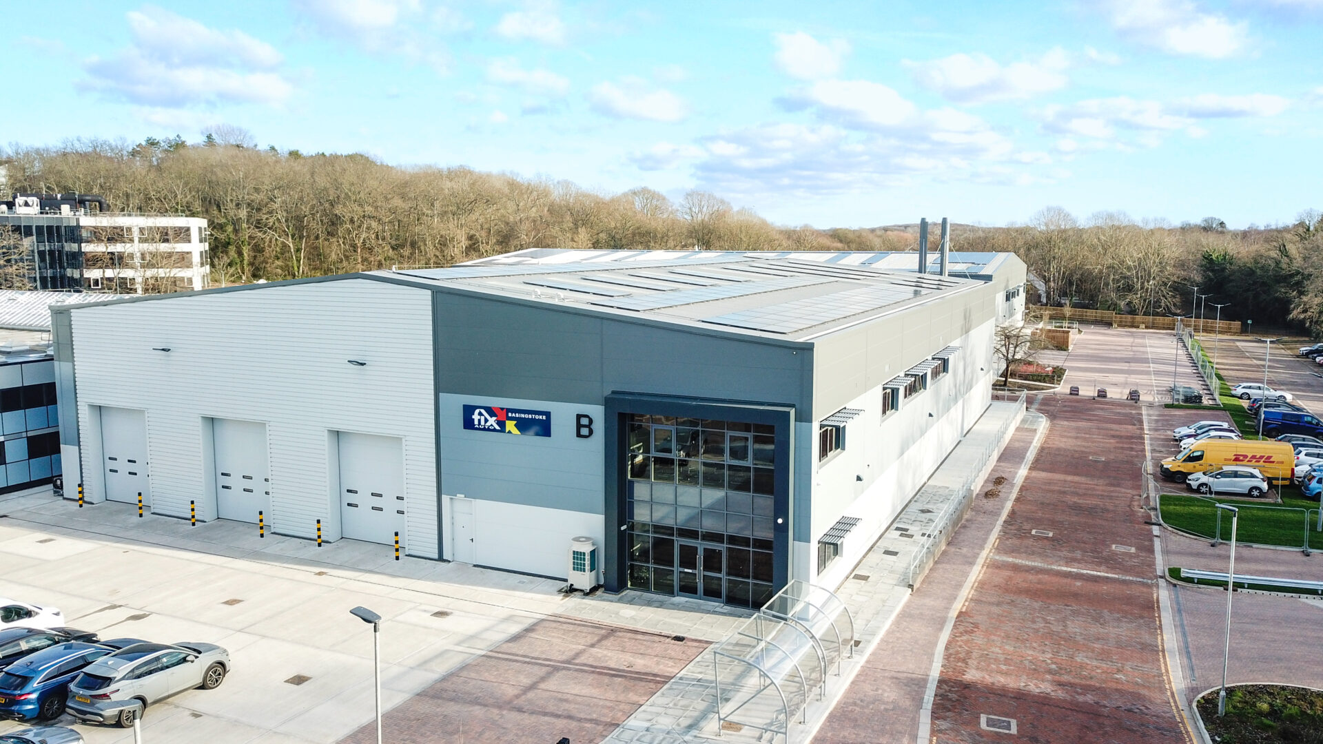 Modern Fix Auto repair facility with white and grey exterior, loading bays and entrance, surrounded by parked vehicles and…
