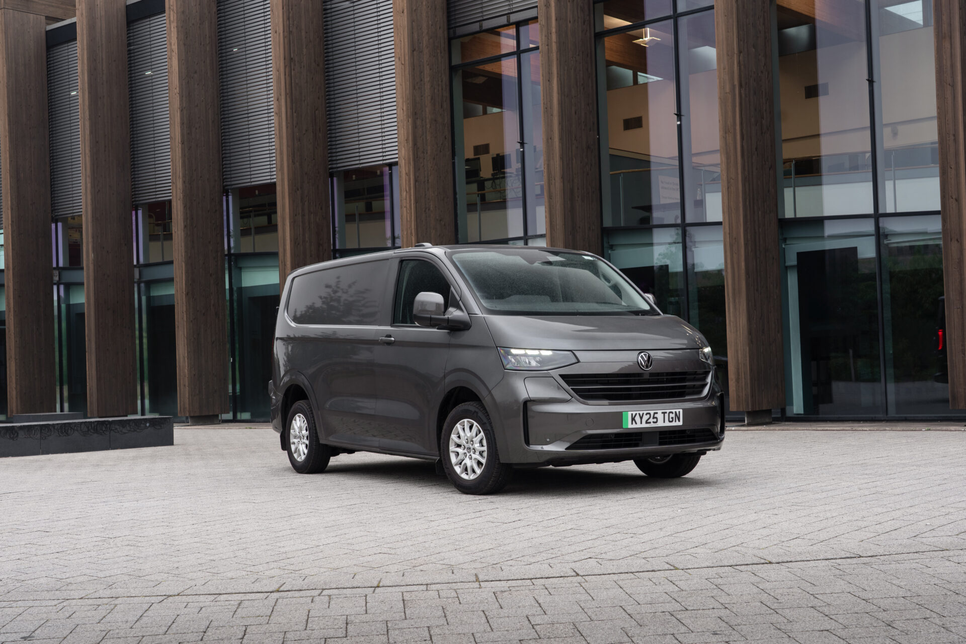 Grey Volkswagen van parked outside modern building with wooden and glass facade.
