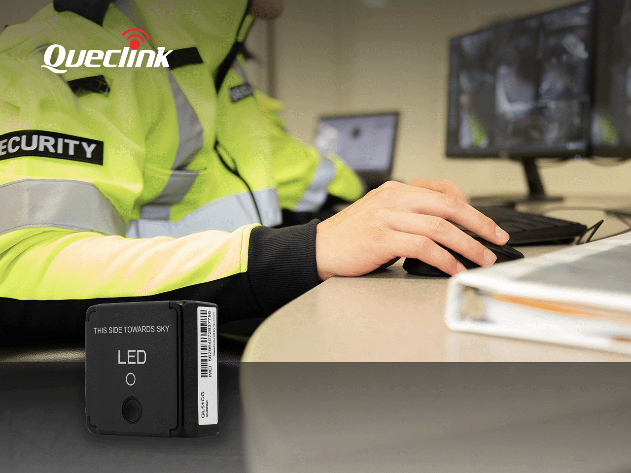 Security personnel in high-visibility jacket operating computer at desk with Queclink GPS tracker device displayed in…