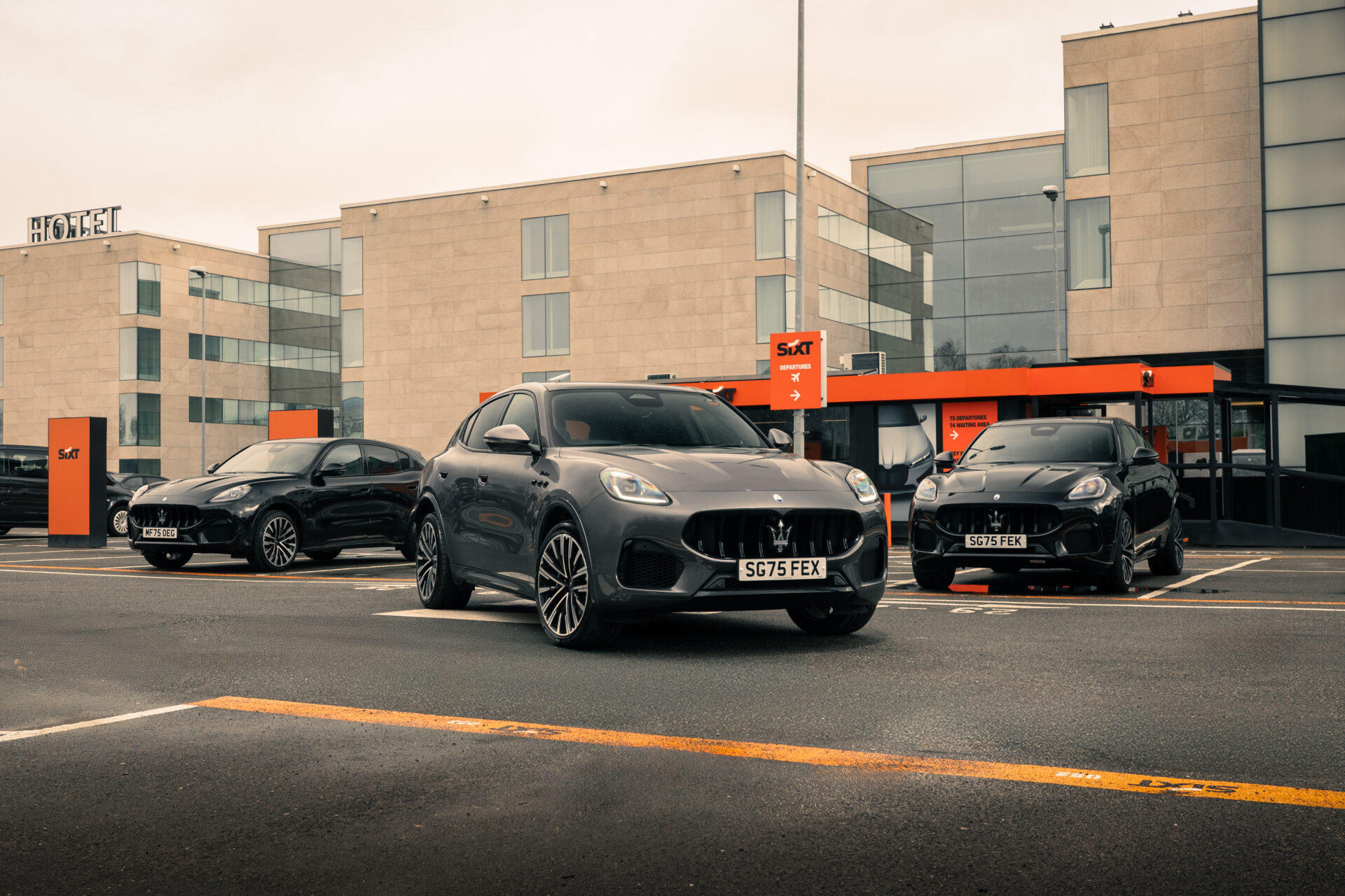 Three Maserati Grecale Modena vehicles parked in front of modern residential building with orange Sixt signage.
