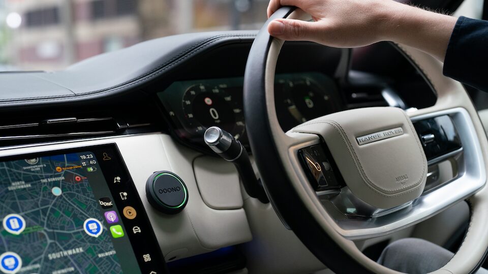 Driver's hand on steering wheel of modern car with touchscreen dashboard displaying navigation map.
