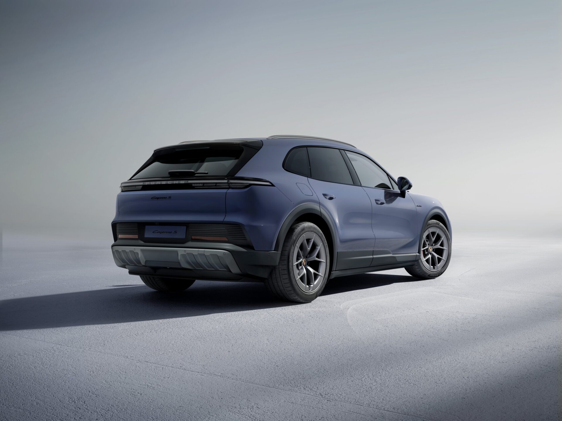 Blue Porsche Cayenne S Electric SUV parked on white surface, rear three-quarter view.