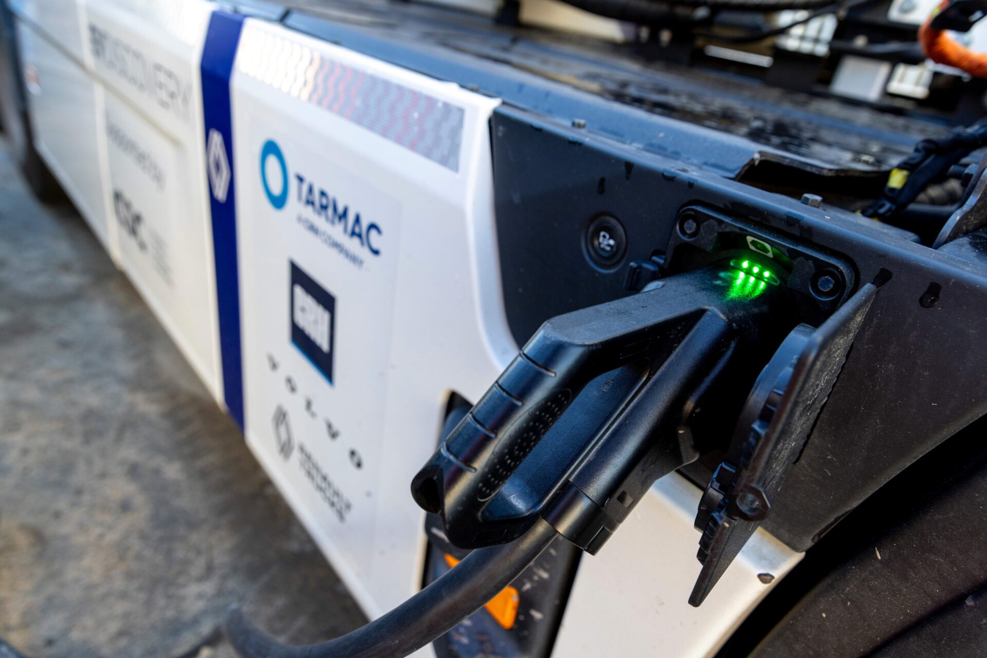Tarmac electric vehicle charging cable connected to truck charging port with green status indicator lit.