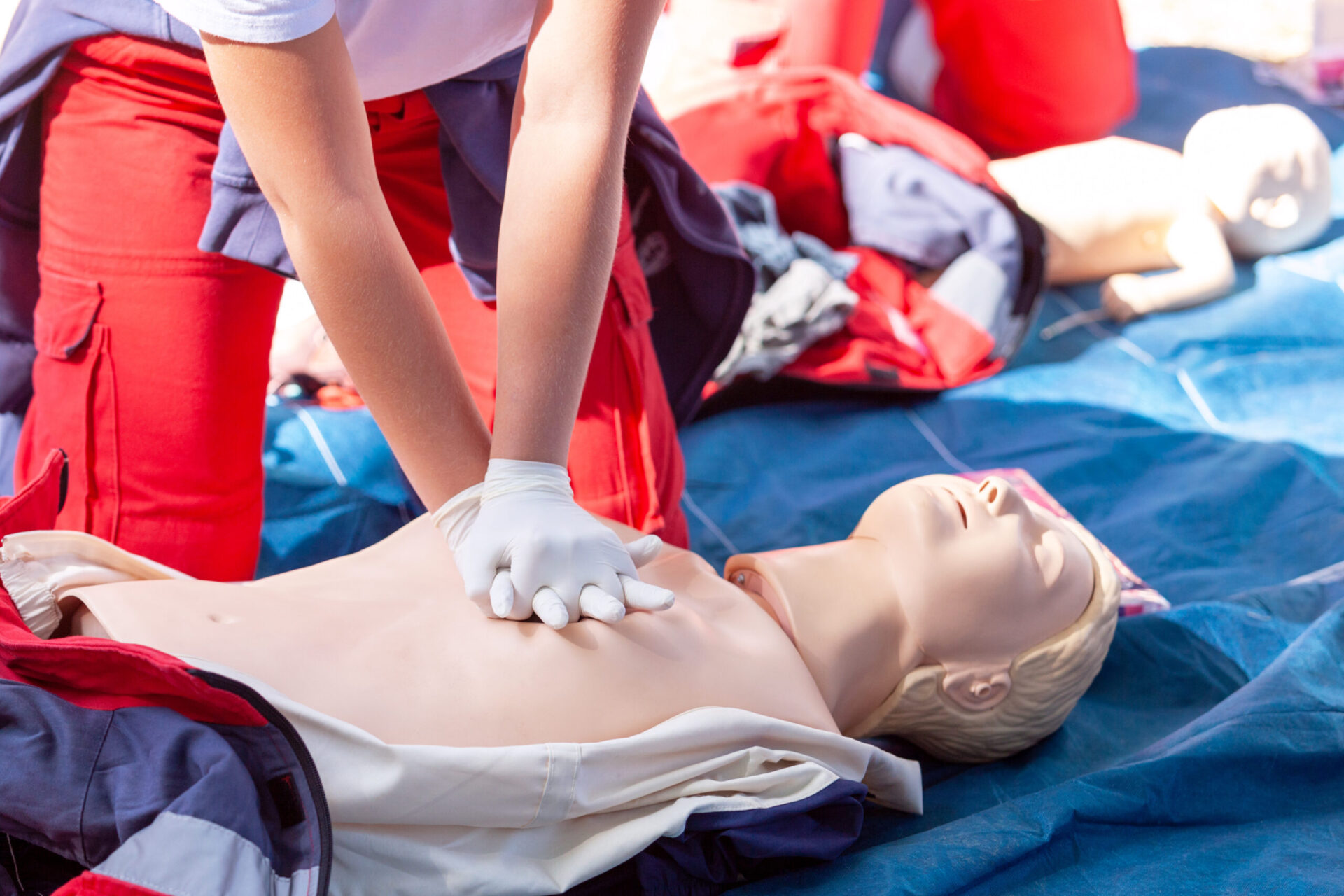 First aider performing chest compressions on CPR training mannequin during emergency response course.